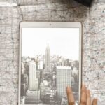 City Map - Flat Lay Photography of Person Touching Silver Ipad on World Map Chart Beside Black Hat