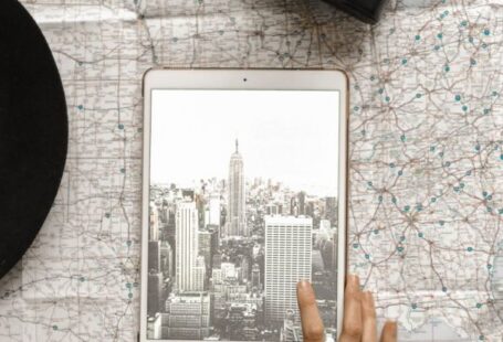 City Map - Flat Lay Photography of Person Touching Silver Ipad on World Map Chart Beside Black Hat