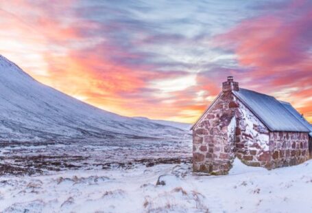 Slopes - Brown House Surrounded by Snow Covered Field Near Snow Covered Mountain Under Yellow Blue and Orange Sunset