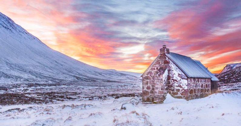 Slopes - Brown House Surrounded by Snow Covered Field Near Snow Covered Mountain Under Yellow Blue and Orange Sunset