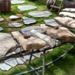 Thematic Mapping - Thematic garden with big stones and hammers on metal rack near lush potted plants on grassland on sunny day