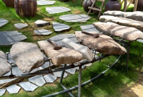 Thematic Mapping - Thematic garden with big stones and hammers on metal rack near lush potted plants on grassland on sunny day