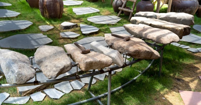 Thematic Mapping - Thematic garden with big stones and hammers on metal rack near lush potted plants on grassland on sunny day