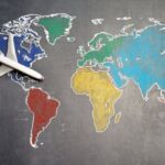 Population Density Map - Top view of crop anonymous person holding toy airplane on colorful world map drawn on chalkboard