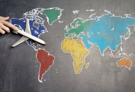 Population Density Map - Top view of crop anonymous person holding toy airplane on colorful world map drawn on chalkboard