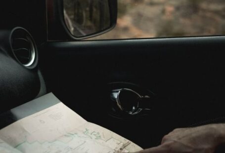 Cartography - Crop faceless male traveler sitting in car and looking route in map during journey