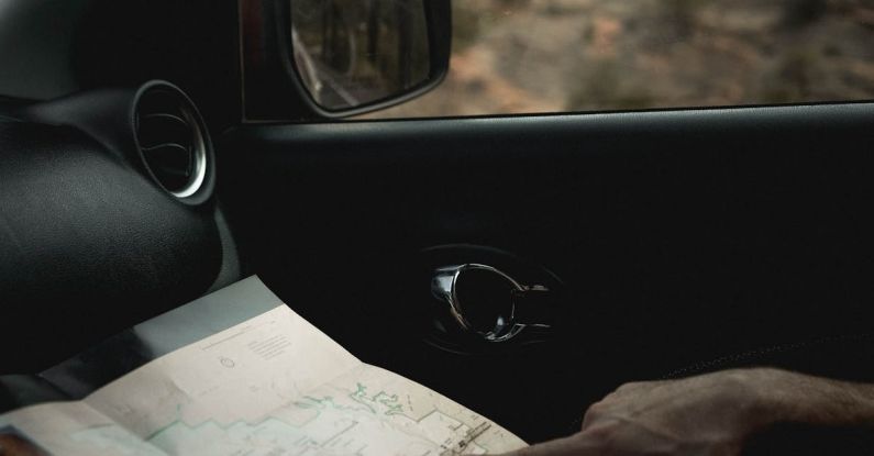 Cartography - Crop faceless male traveler sitting in car and looking route in map during journey